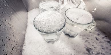 Three glasses overflowing with soap suds in a sink.