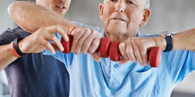 Senior man lifting dumbbells with assistance from a trainer.