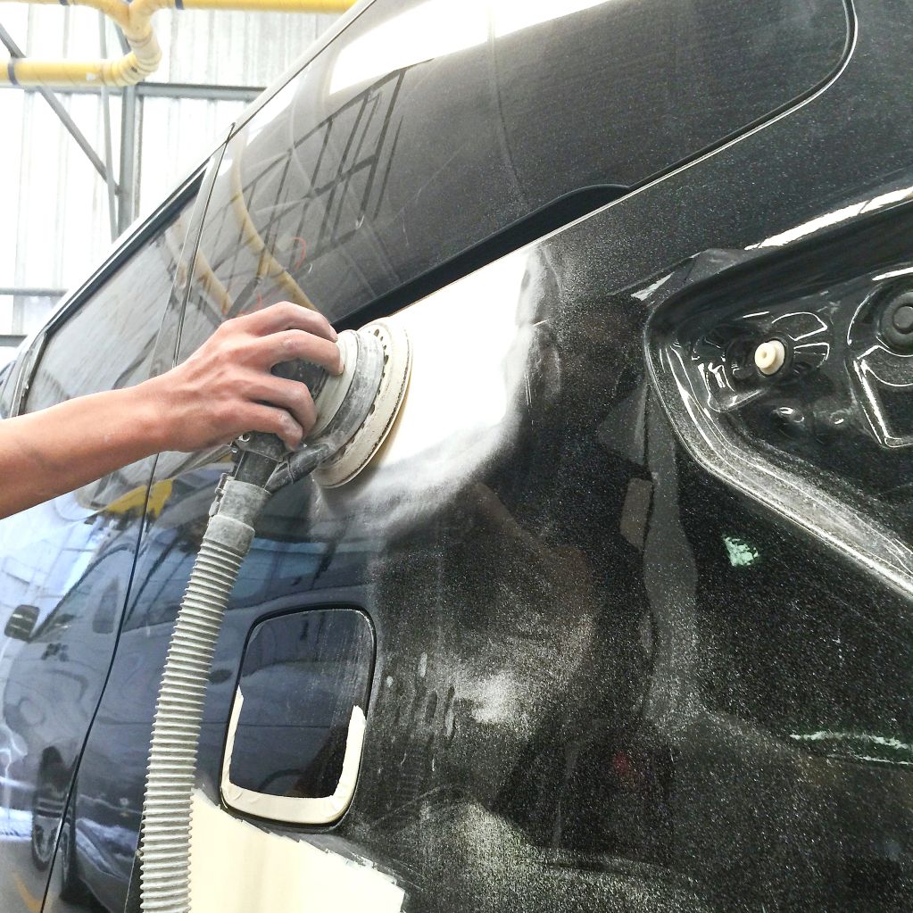 Hand sanding a black car body for repair and painting.
