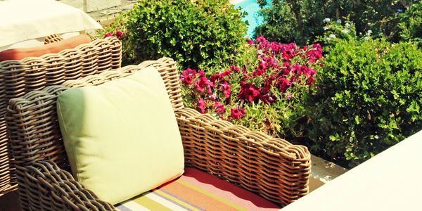 Wicker chair with cushion by vibrant garden flowers and greenery.
