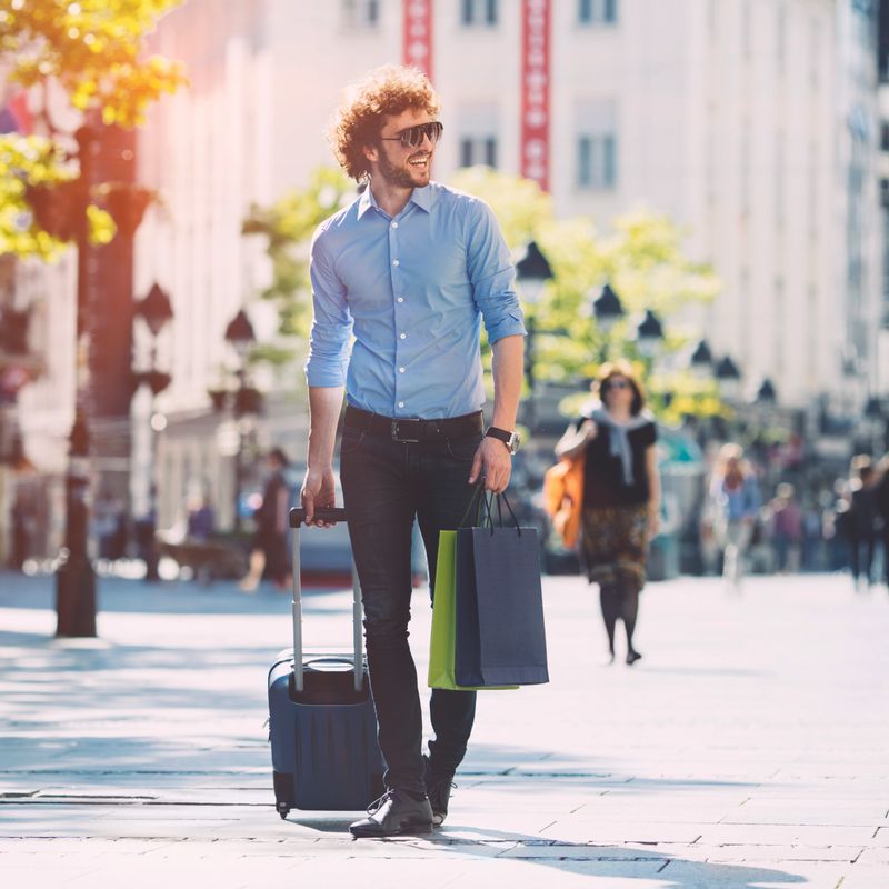 Cheerful male shopping in the city. Walking down the street with shopping bags and luggage.