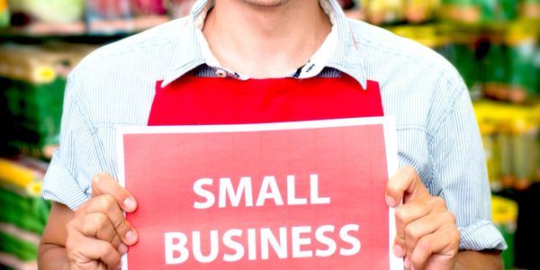 Person holding a sign that reads 'SMALL BUSINESS' in a store setting.