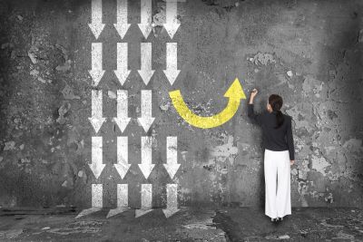 Woman drawing a yellow arrow turning upward against downward white arrows.