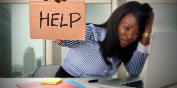 Stressed woman holding a HELP sign at her desk.