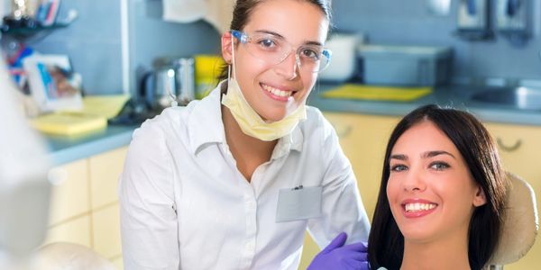 Dentist in protective gear smiling with a female patient in a clinic.