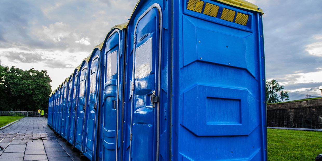 A row of blue portable toilets with yellow tops lined up on a paved path.