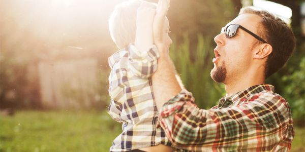 Father joyfully lifting his child outdoors in sunlight.
