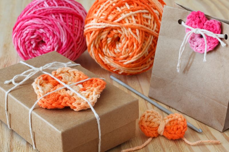 Handmade colorful crochet flowers and heart for decoration of gift with skein on wooden table. Selective focus