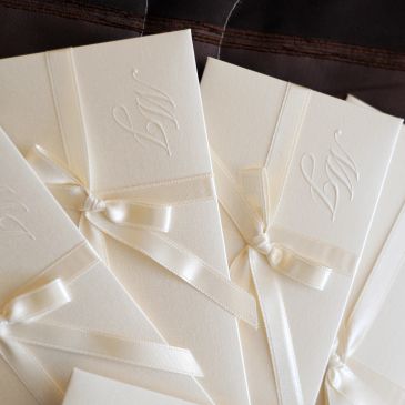 Elegant white invitations with embossed initials and satin ribbons.