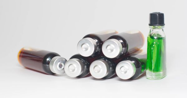 Vials of dark liquid and one vial with green liquid on a white background.