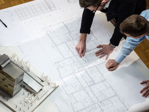 Two people examining architectural plans with a model building.