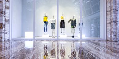 Fashionable mannequins display colorful clothing in a sleek store window with marble flooring.