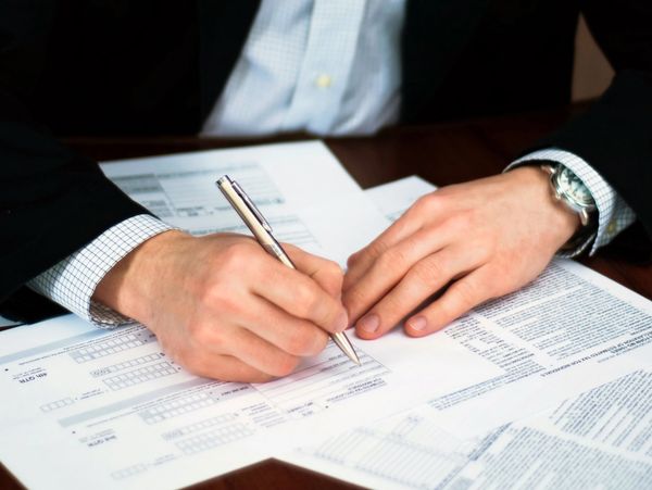 Person in formal attire filling out official documents with a pen.