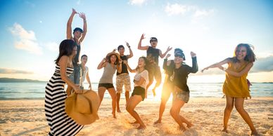 A group of friends joyfully jumping and dancing on a sunny beach at sunset.