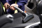 Person vacuuming a car seat with a handheld vacuum cleaner.