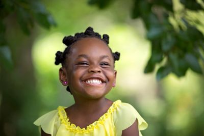 Une petite fille souriante en robe jaune.