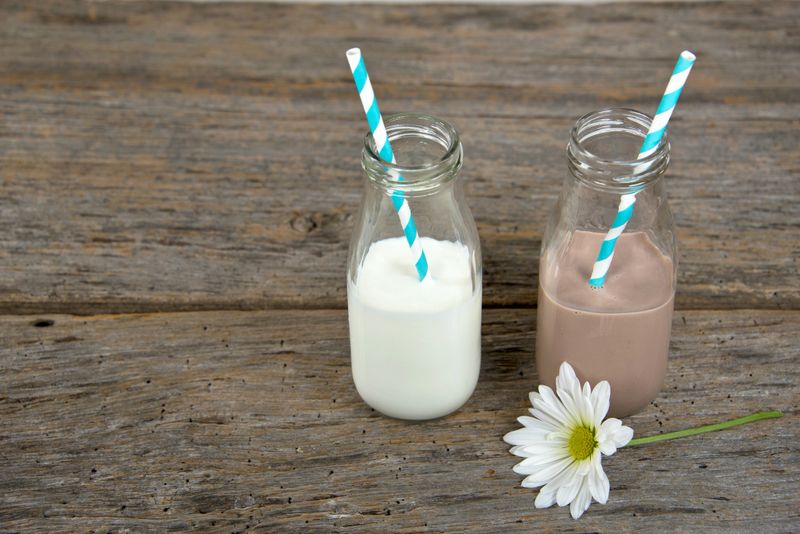 White and chocolate milk in glass retro bottles with striped straws and white daisy on rustic wood.