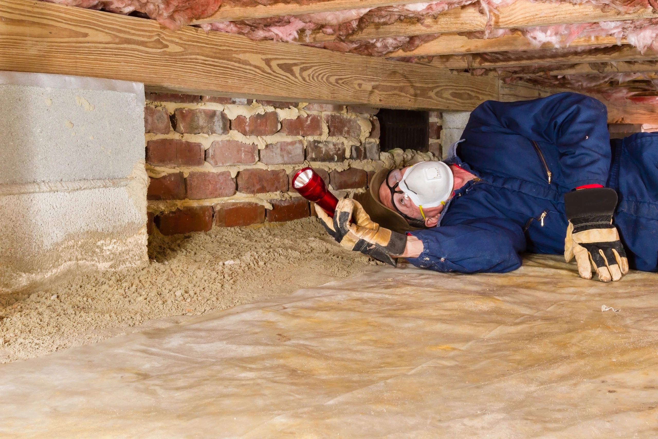 Man inspecting a crawl space with flashlight and mask.