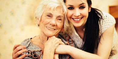 A young woman embraces an elderly woman, both smiling warmly.