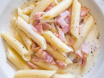 Creamy penne pasta with ham and bacon bits, sprinkled with black pepper.