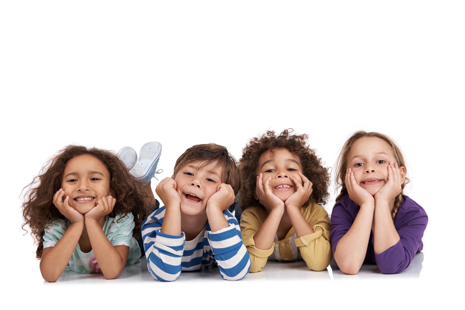 Four diverse children lying on their stomachs, smiling with hands on their cheeks.