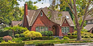 Charming brick house with lush greenery and trees in a quiet neighborhood.