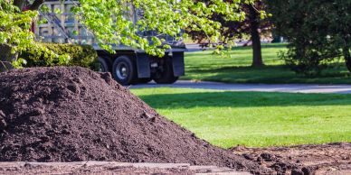 Pile of soil with a truck and greenery in background.