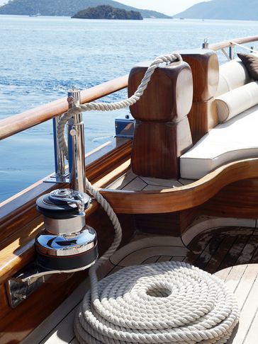 Coiled rope and polished winch on a wooden yacht deck by the sea.