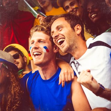 Friends enjoying a sports event with painted faces and cheering.