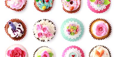 Twelve beautifully decorated cupcakes with colorful floral designs on white background.