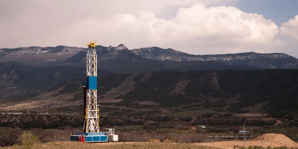 Oil drilling rig set against mountainous landscape under cloudy sky.