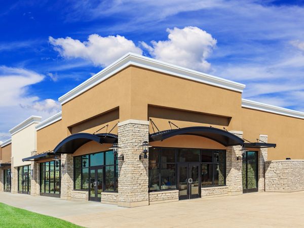 New commercial building with stone pillars and large glass windows under a blue sky.