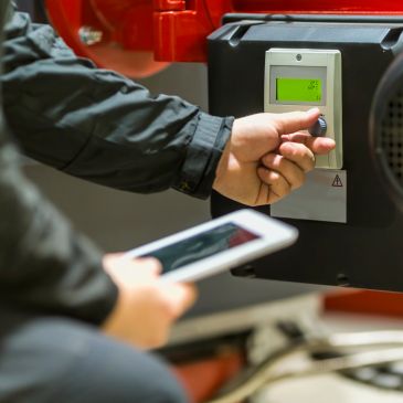 Technician operating a machine control panel while holding a tablet.