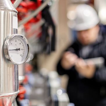 Temperature gauge on industrial equipment with worker in background.