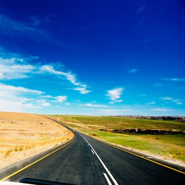 A winding road stretches through contrasting dry and green fields under a vivid blue sky.