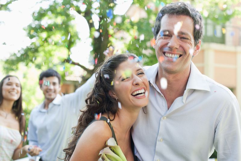 Couple outdoors at party carrying flowers and having confetti thrown at them