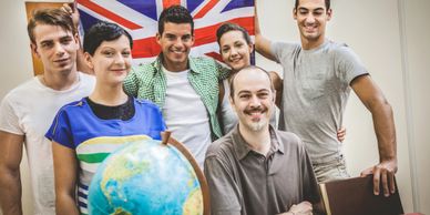 A group of young people with a globe and a British flag, smiling in a classroom.