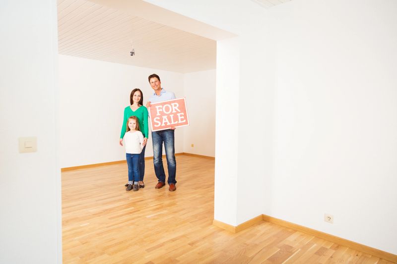 family in an empty apartment, holding "for sale" sign