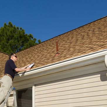 Man inspecting a house roof while standing on a ladder with a clipboard.