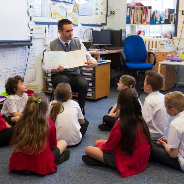 Teacher reading a book to young students in a classroom.