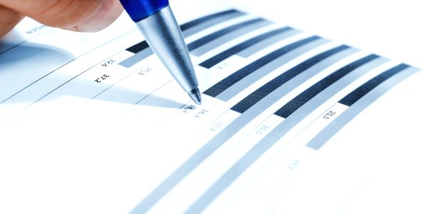 Close-up of hand with pen pointing to a bar chart on paper.