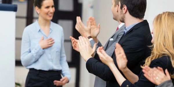 Colleagues applauding a woman in a professional setting.