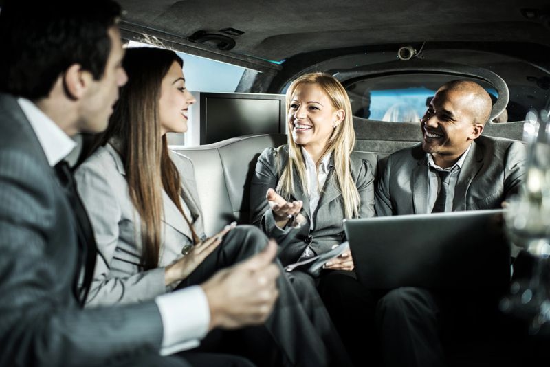Four cheerful business people sitting in a limousine and communicating.  