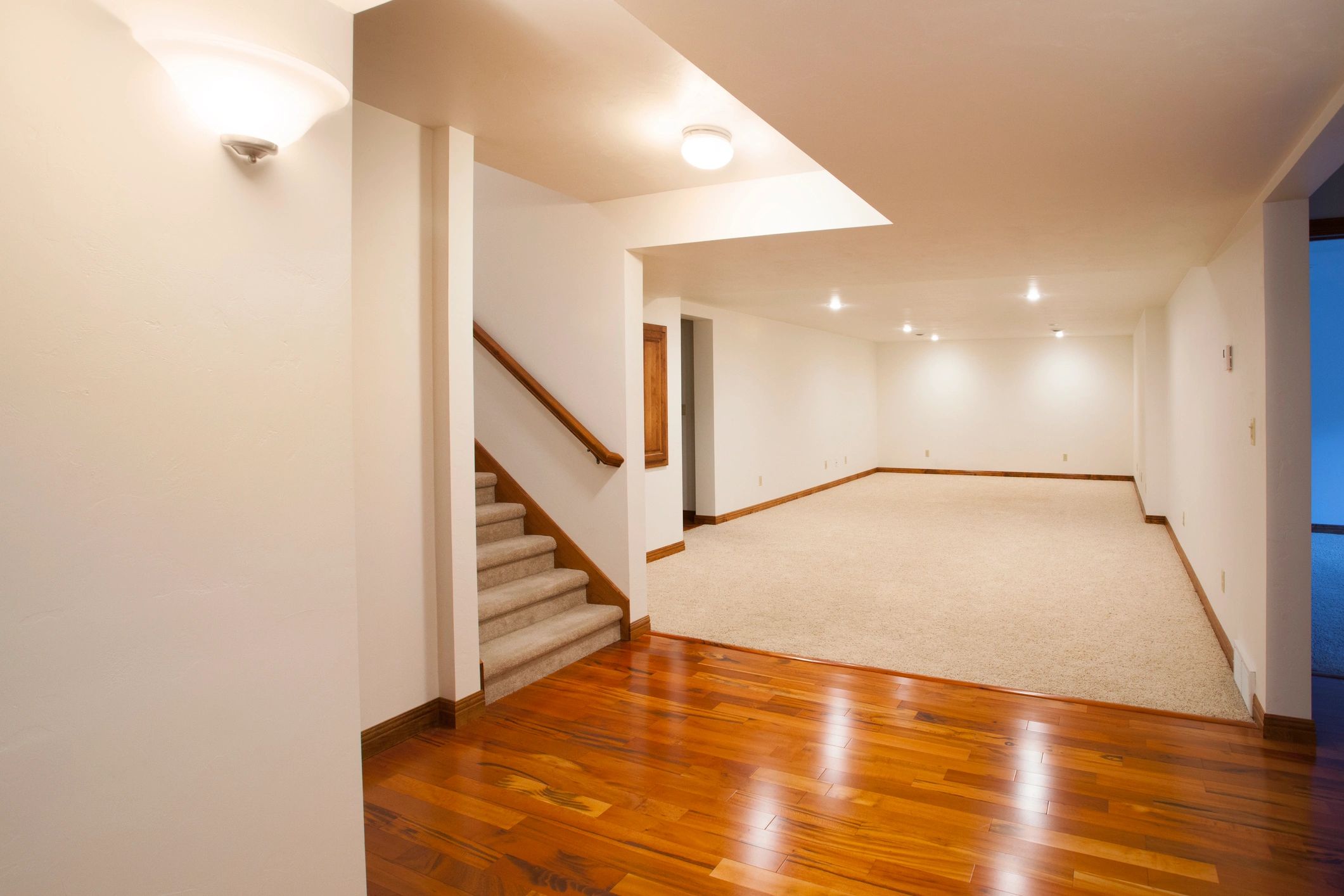Empty basement with wooden floor and carpeted stairs.