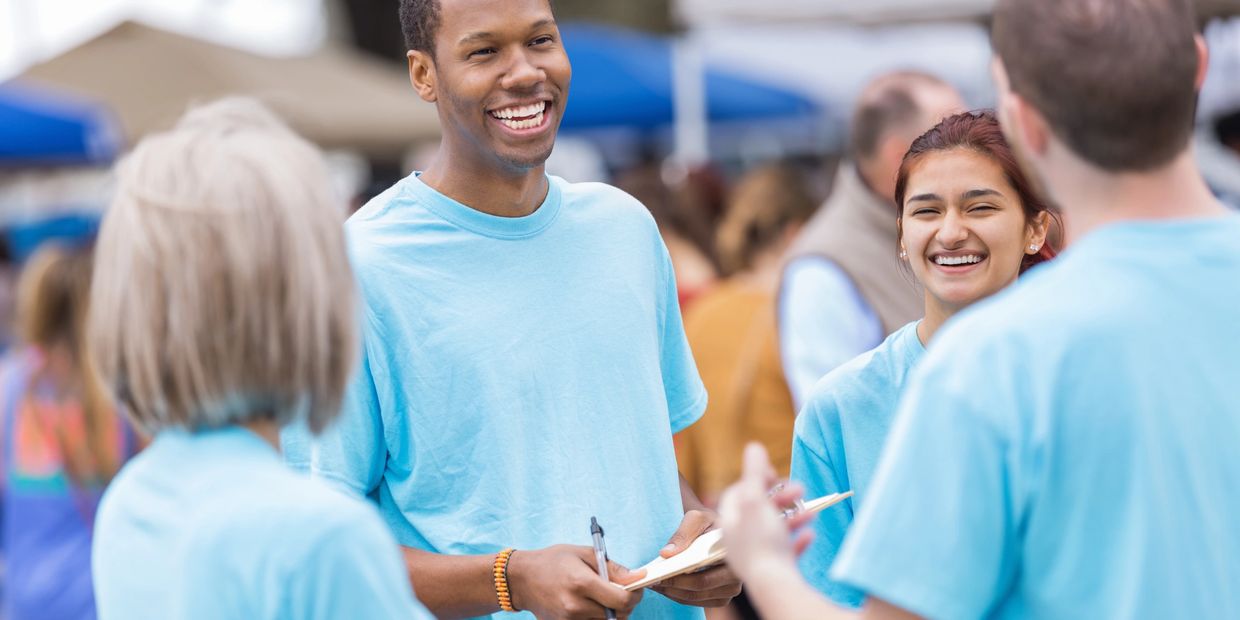 Young volunteers in light blue shirts laughing and talking outdoors.