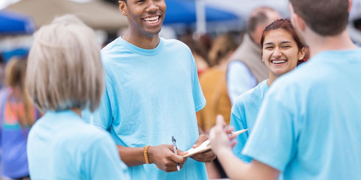 Young volunteers in light blue shirts laughing and talking outdoors.