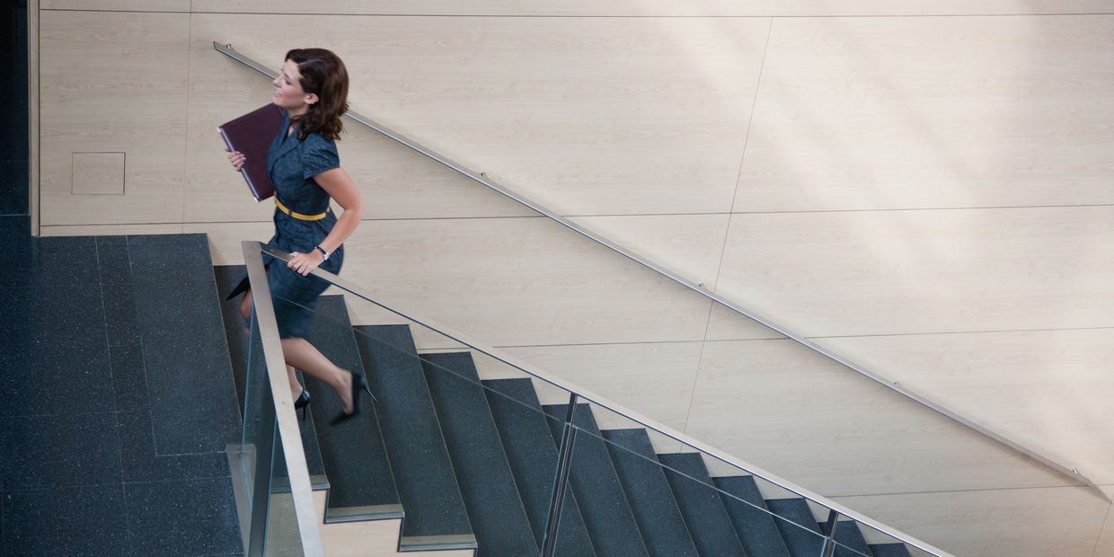 A woman in business attire climbs stairs holding a folder.