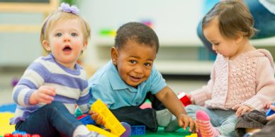 Three toddlers playing together with colorful blocks indoors.