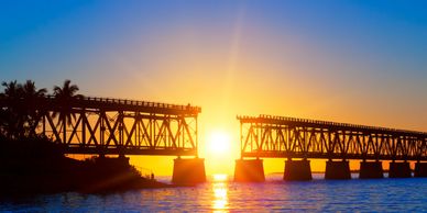 Sunset view of a broken iron bridge over water with a clear sky.