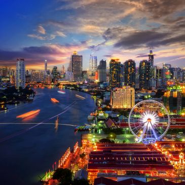 City skyline with river and illuminated ferris wheel at dusk.